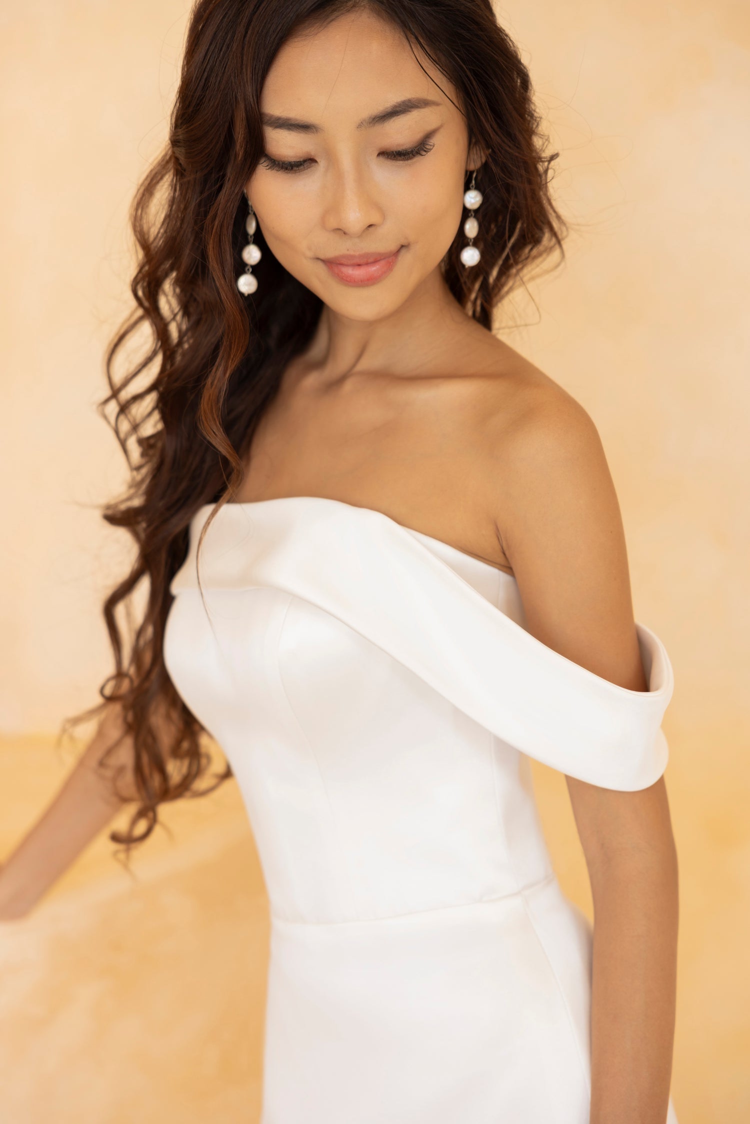 Close-up detail of Indy gown's asymmetrical off-shoulder neckline and structured satin fabric