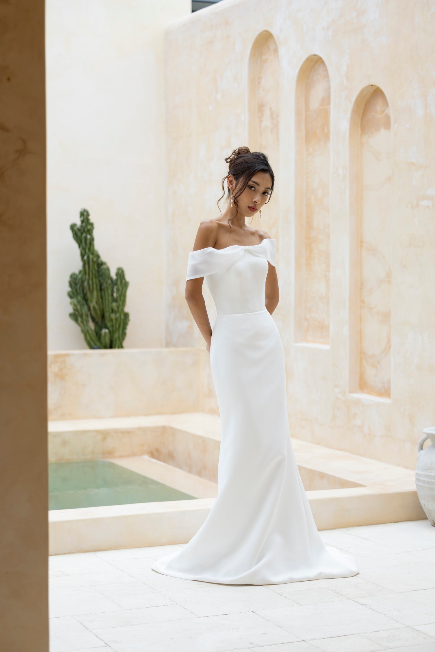 Bride in Robin off-shoulder crepe wedding gown by TheWolfandLily, front view with organza bow detail