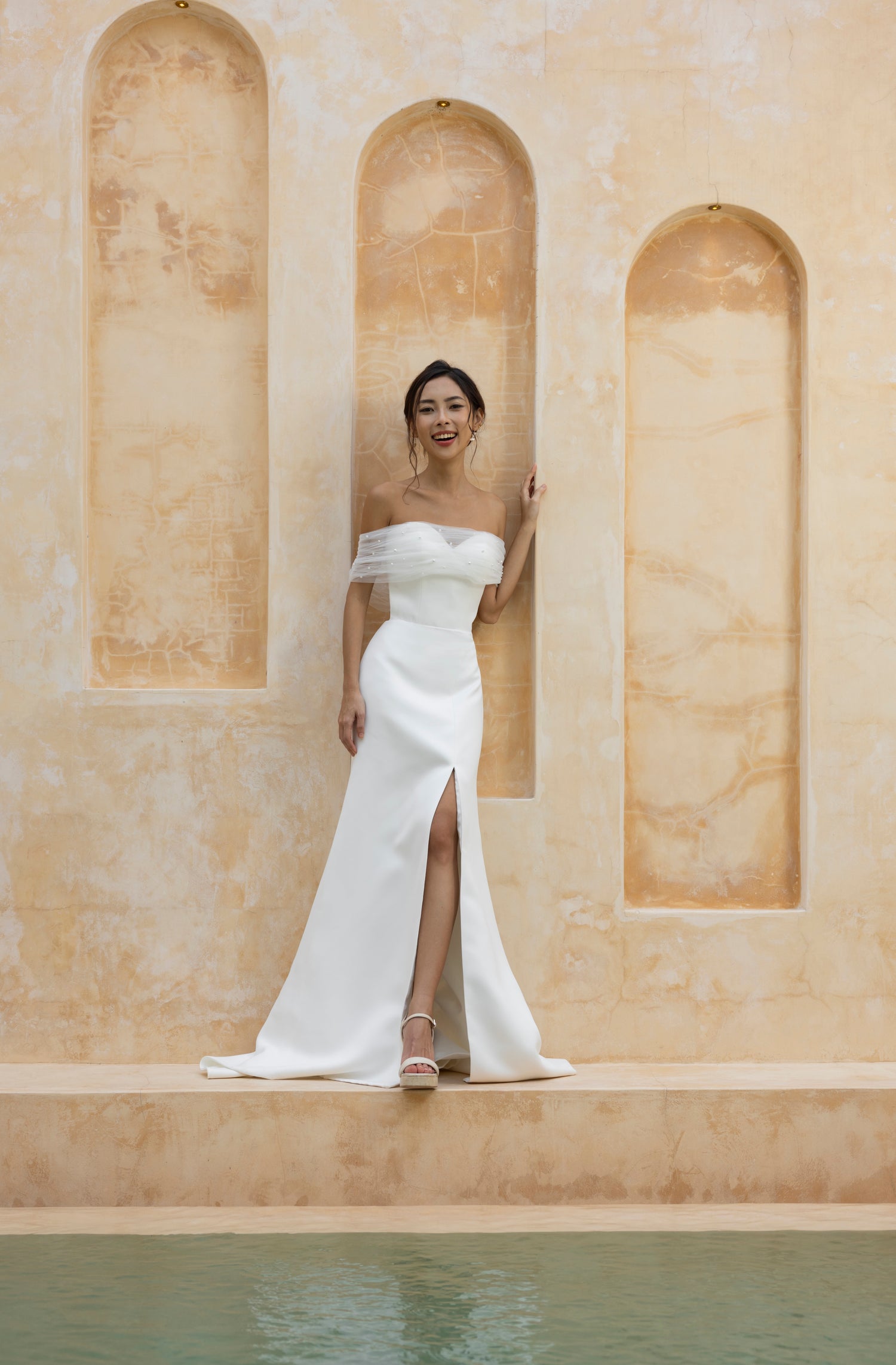 Bride in the Teagan wedding gown by TheWolfandLily, featuring a sweetheart neckline, front slit, and detachable pearl-embellished tulle wrap.