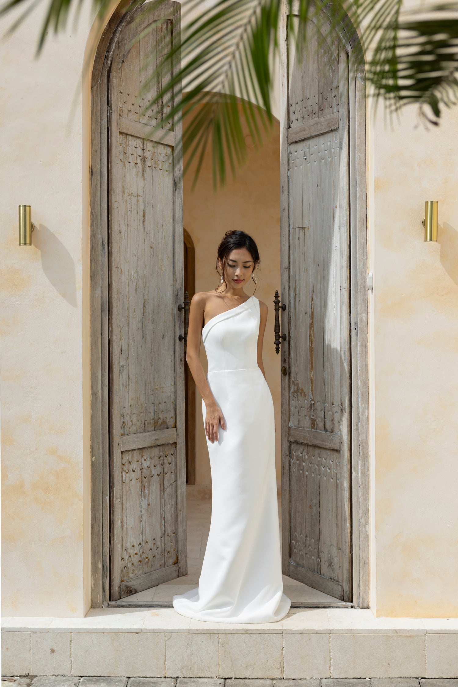 Bride in The Wolf and Lily Isla crepe gown with asymmetric neckline and column silhouette, posing in natural light.