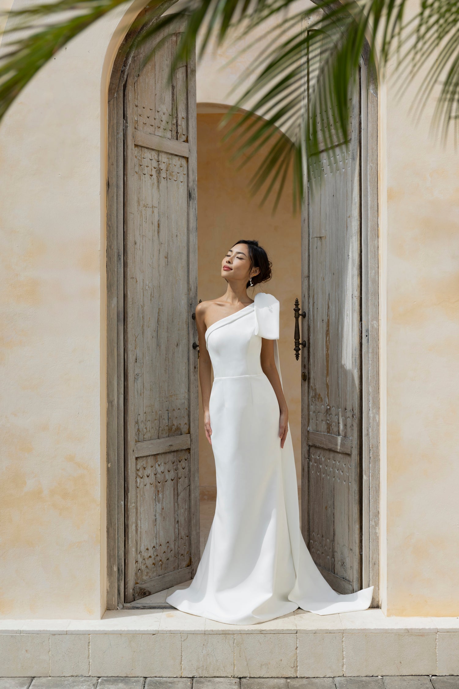 Minimalist crepe wedding dress with asymmetric neckline and detachable shoulder bow by The Wolf and The Lily.
